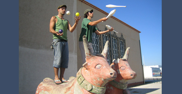 Two men juggling while standing on statues of bulls.